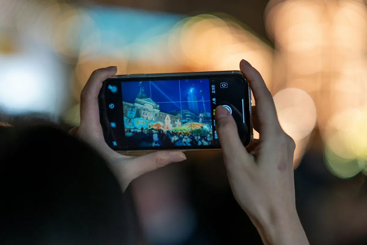 Close-up of hands holding a smartphone to take a photo of an illuminated city scene at night