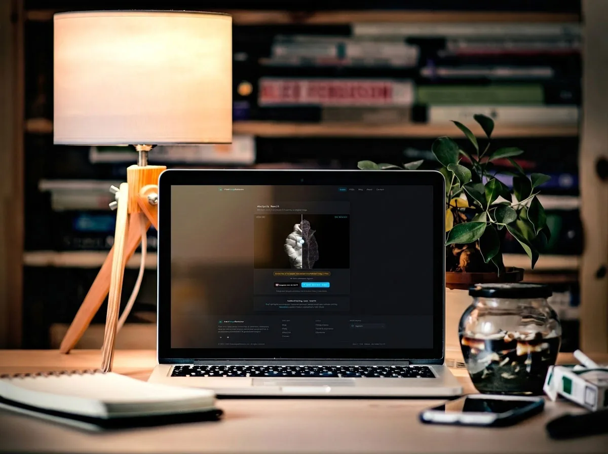 Open laptop on a cozy, warmly lit desk surrounded by a lamp, plant, and bookshelf