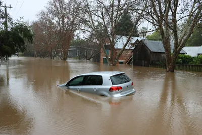 A silver hatchback partially submerged in deep, murky floodwaters on a residential street