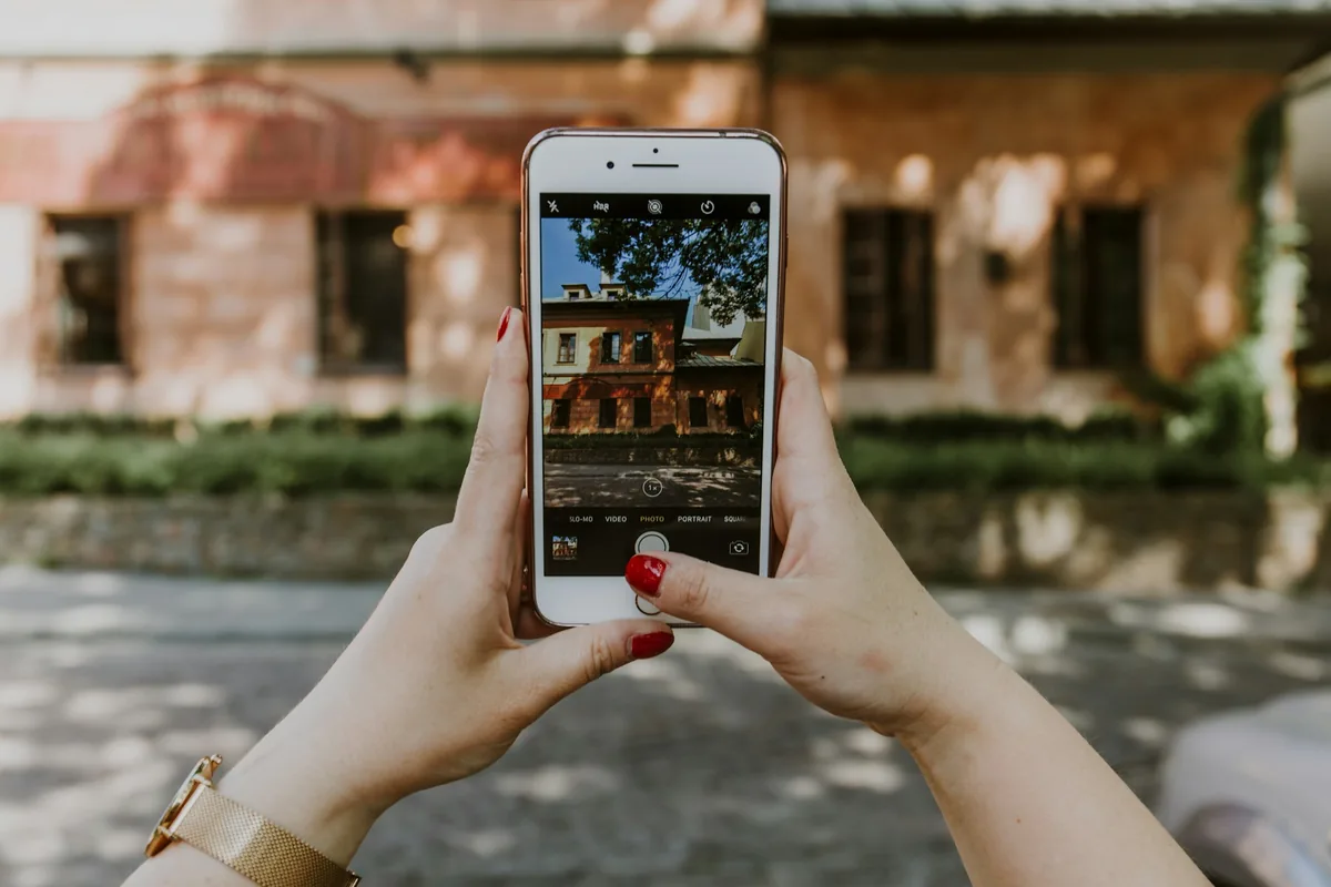Close-up of hands with red nail polish holding a smartphone to take a vertical photo.