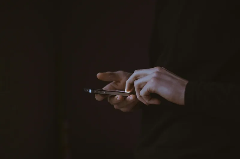 Close-up of hands typing on a glowing smartphone in the dark