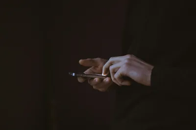Close-up of hands typing on a glowing smartphone in the dark
